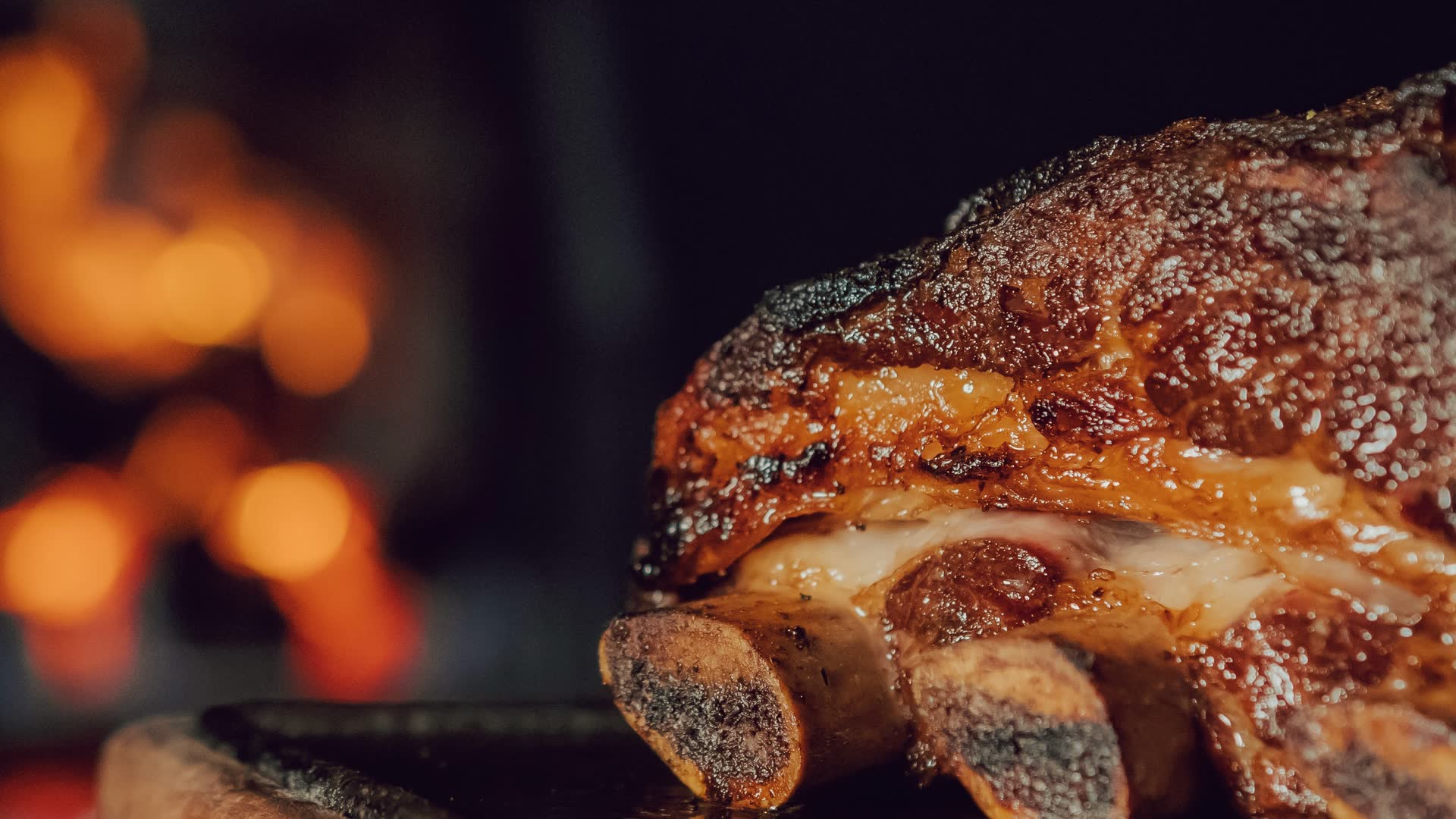 Costillar de asado de tira a las brasas, con el fuego de la parrilla desenfocado al fondo