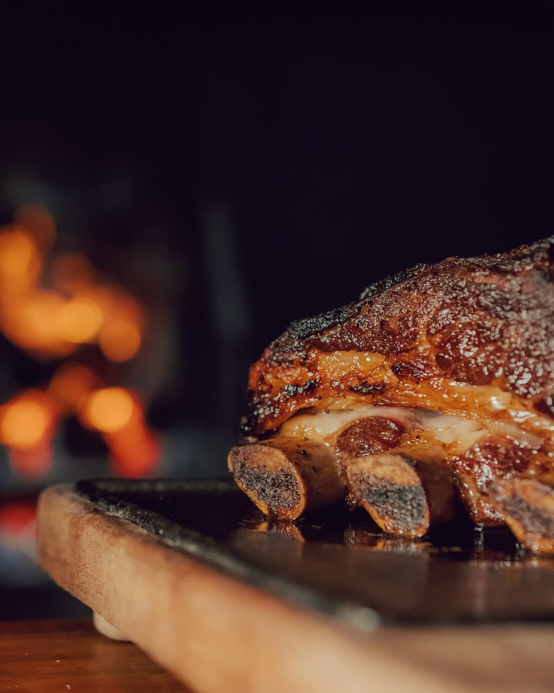 Costillar de asado de tira a las brasas, con el fuego de la parrilla desenfocado al fondo