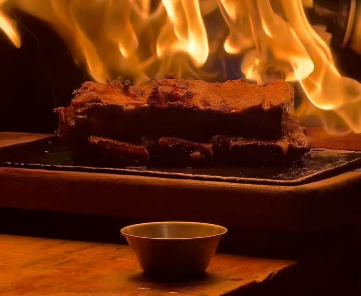 Corte servido en plancha de fierro bajo llamas altas, con un pocillo de salsa